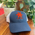 Navy blue cap with red logo and text on a wooden surface with plants in the background